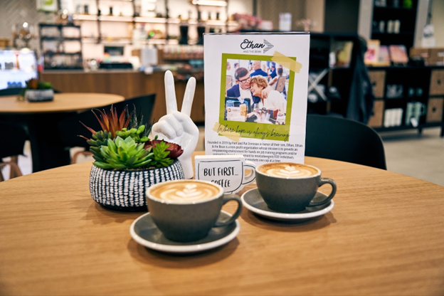 Two cups of coffee on a table with a plant and a sign in the background.
